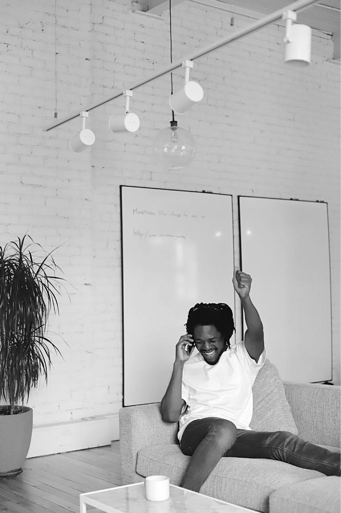 Jeune homme heureux au téléphone cellulaire dans son appartement logement en ville accompagnement lancement solopreneur